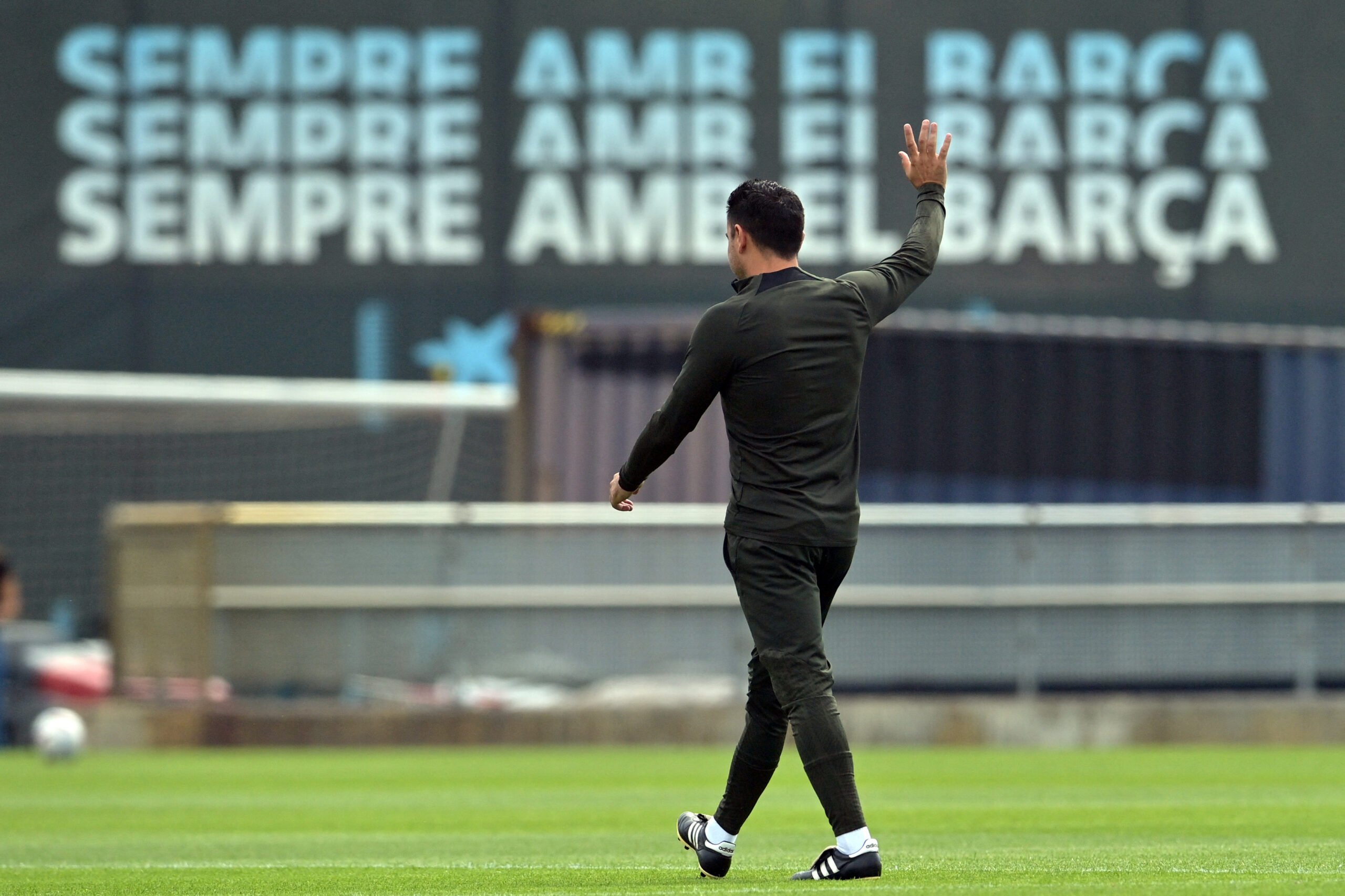 TOPSHOT - Barcelona Spanish coach Xavi waves during a training session at the Joan Gamper training ground in Sant Joan Despi, near Barcelona, on May 25, 2024. Text in the background reads in Catalan "Always with Barcelona".